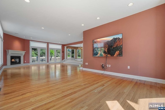 unfurnished living room with french doors, light wood-type flooring, and an inviting chandelier