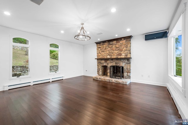 unfurnished living room featuring a wall mounted air conditioner, dark wood-type flooring, a baseboard heating unit, a chandelier, and a stone fireplace