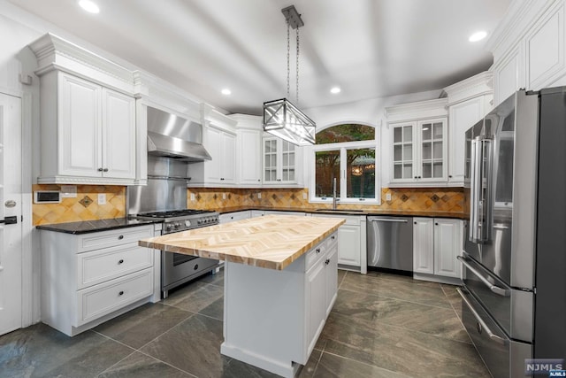 kitchen with butcher block counters, wall chimney exhaust hood, hanging light fixtures, a kitchen island, and high end appliances