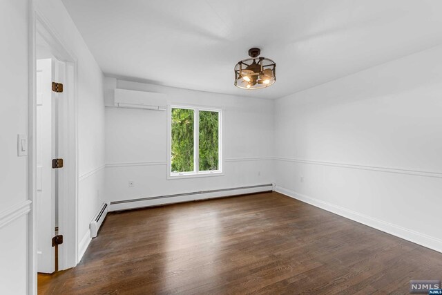 spare room with an inviting chandelier, a wall unit AC, baseboard heating, and dark wood-type flooring