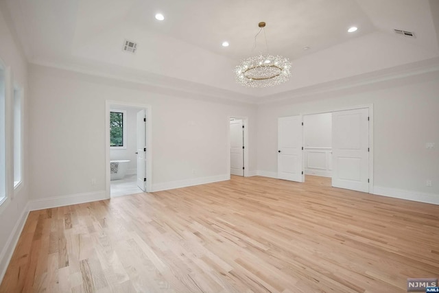 unfurnished bedroom with light wood-type flooring, ensuite bathroom, a tray ceiling, and a notable chandelier