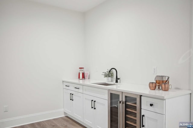 bar with white cabinetry, sink, beverage cooler, and light hardwood / wood-style flooring