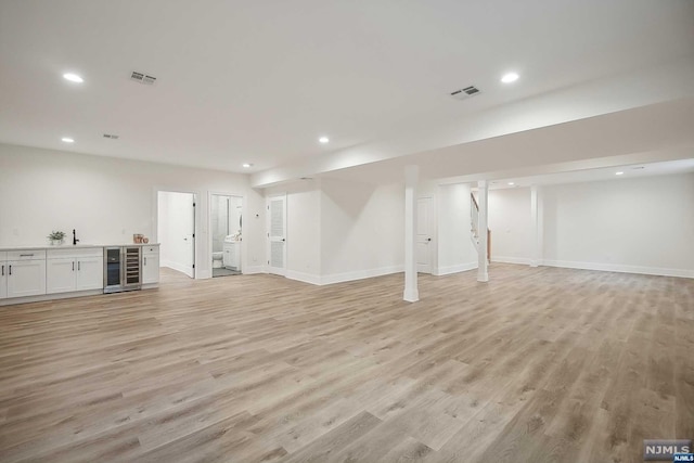 basement with light hardwood / wood-style flooring and beverage cooler