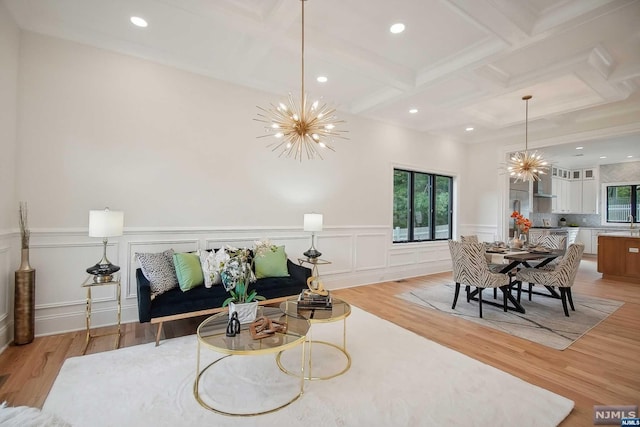 living room featuring beamed ceiling, an inviting chandelier, light hardwood / wood-style flooring, and coffered ceiling