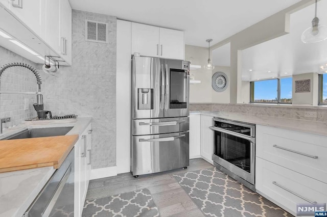 kitchen with stainless steel appliances, sink, pendant lighting, light hardwood / wood-style flooring, and white cabinetry