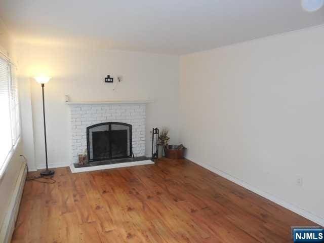 unfurnished living room featuring hardwood / wood-style floors, baseboard heating, and a brick fireplace