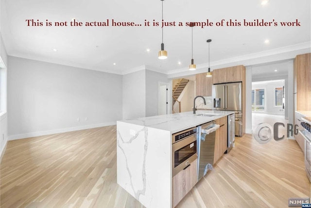 kitchen with a kitchen island with sink, hanging light fixtures, light wood-type flooring, light stone counters, and stainless steel appliances