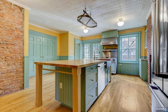 kitchen featuring stainless steel appliances, wood counters, green cabinets, brick wall, and light hardwood / wood-style floors