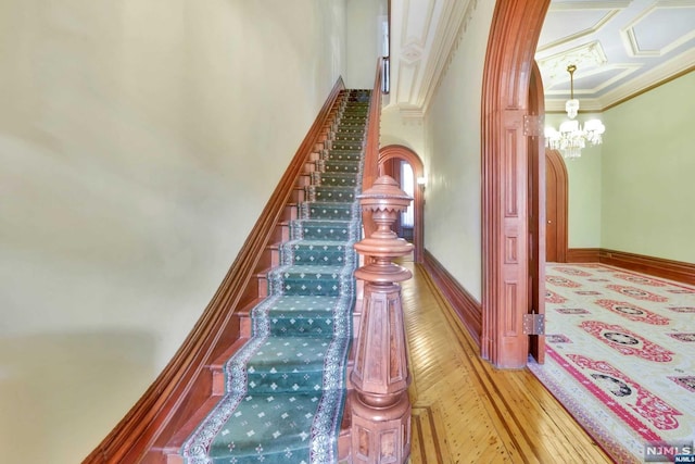 stairs featuring hardwood / wood-style floors, ornamental molding, and a notable chandelier