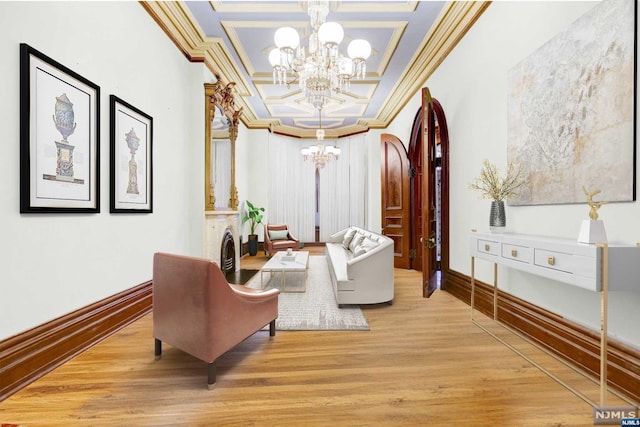 living area with light hardwood / wood-style floors, ornamental molding, a tray ceiling, and an inviting chandelier