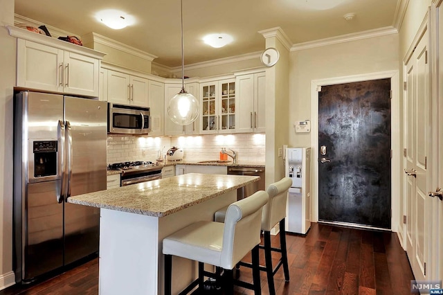 kitchen featuring dark hardwood / wood-style flooring, light stone counters, stainless steel appliances, crown molding, and pendant lighting