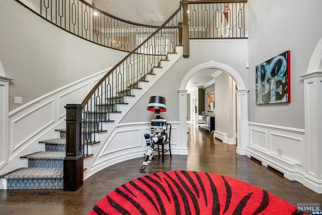 entryway featuring dark hardwood / wood-style floors, a towering ceiling, crown molding, and ornate columns