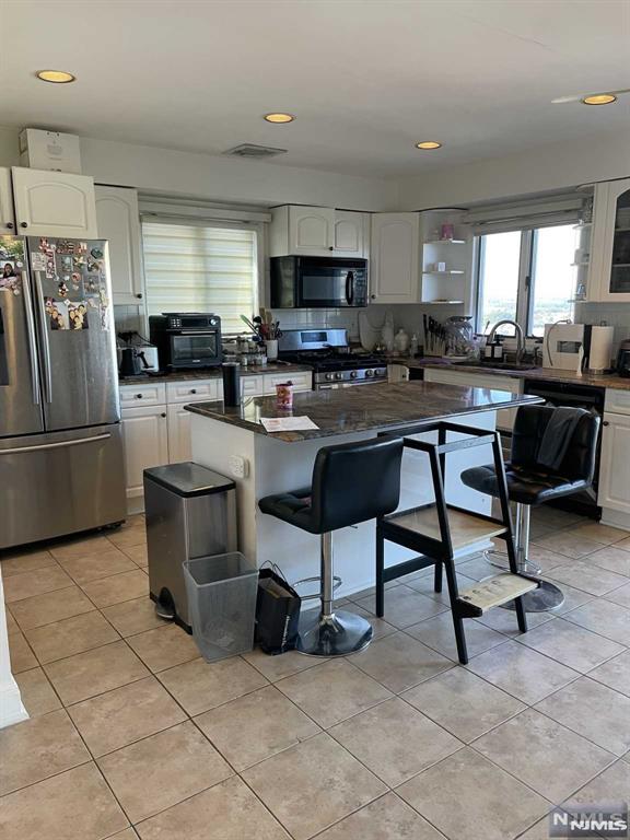 kitchen with light tile patterned floors, appliances with stainless steel finishes, a kitchen island, a kitchen bar, and white cabinetry