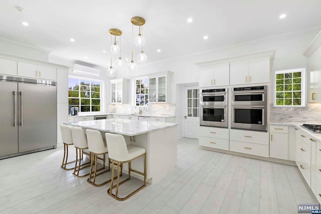 kitchen with stainless steel appliances, a kitchen island, crown molding, decorative light fixtures, and white cabinets