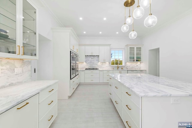 kitchen with light stone countertops, a large island, stainless steel gas cooktop, decorative backsplash, and white cabinets