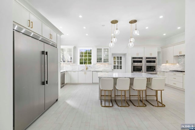 kitchen featuring light stone countertops, appliances with stainless steel finishes, a kitchen island, decorative light fixtures, and white cabinetry