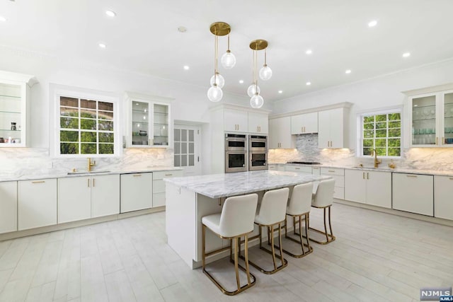 kitchen featuring light stone countertops, a center island, pendant lighting, white cabinets, and appliances with stainless steel finishes