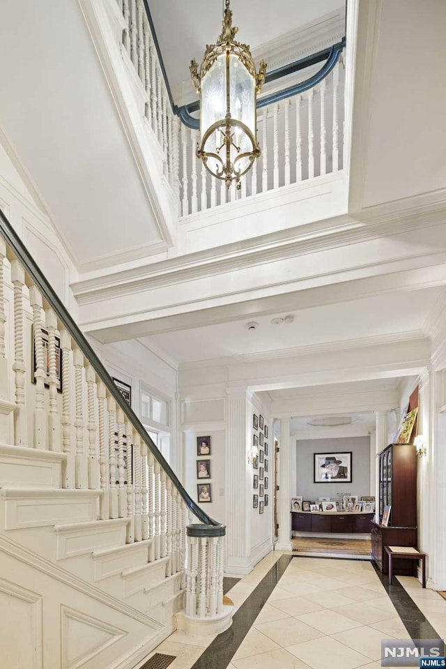 tiled foyer with a chandelier, a high ceiling, and ornamental molding