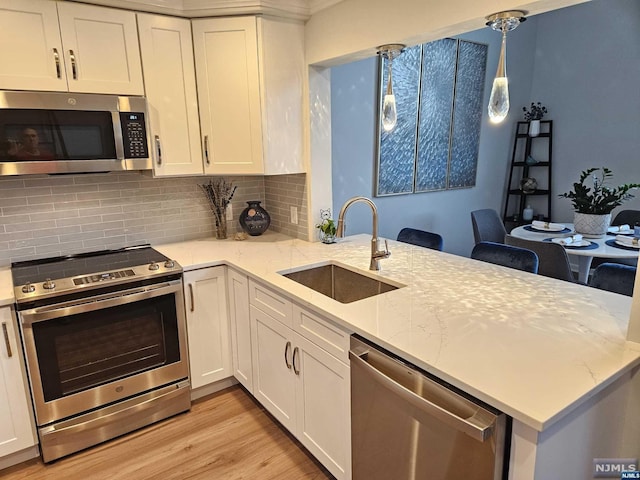 kitchen featuring sink, decorative light fixtures, light stone counters, white cabinetry, and stainless steel appliances