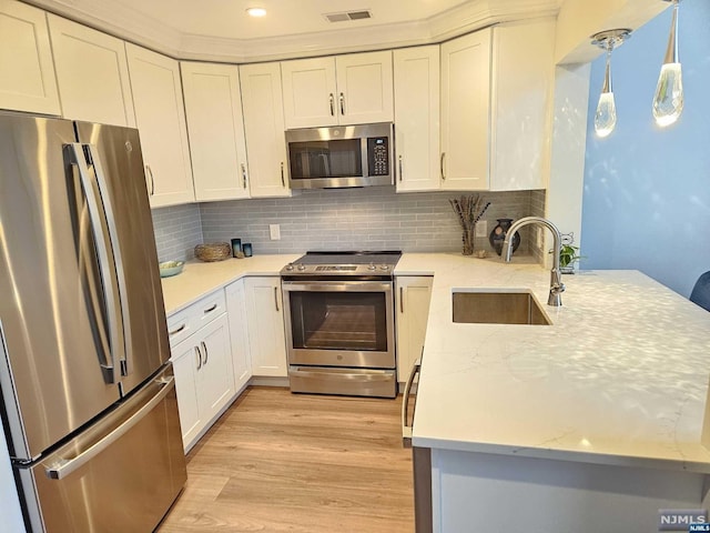 kitchen with light wood-type flooring, stainless steel appliances, sink, pendant lighting, and white cabinetry