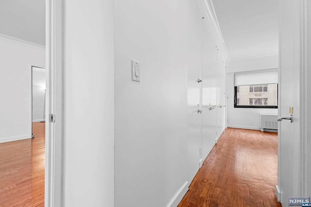 hallway with light wood-type flooring, radiator heating unit, and ornamental molding