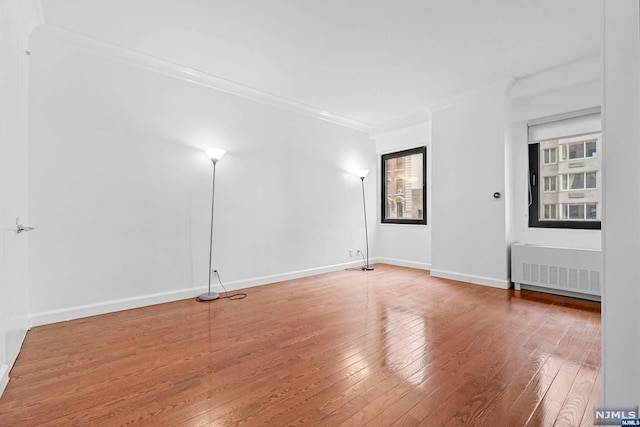 spare room with radiator heating unit, ornamental molding, and wood-type flooring