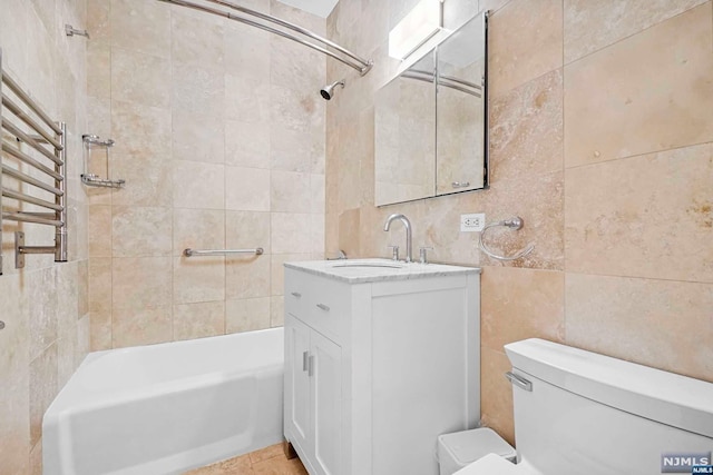 full bathroom featuring vanity, tile patterned floors, tiled shower / bath, toilet, and tile walls