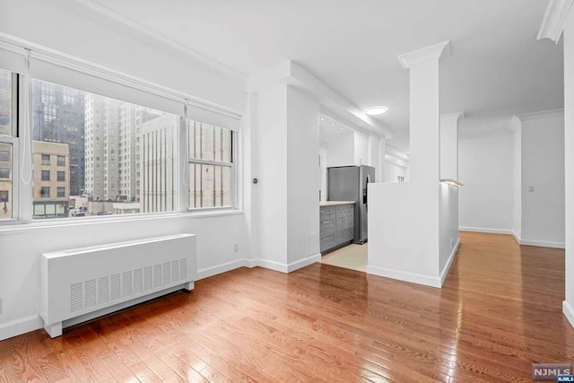 empty room with light hardwood / wood-style flooring, radiator, and ornamental molding