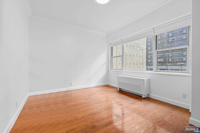 unfurnished room with radiator heating unit, light hardwood / wood-style flooring, and crown molding