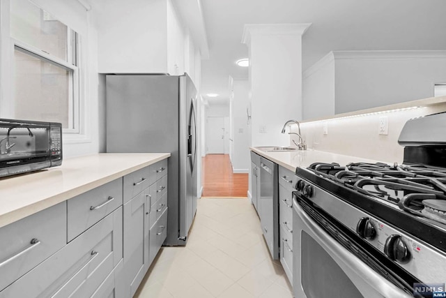 kitchen with appliances with stainless steel finishes, gray cabinets, ornamental molding, and sink