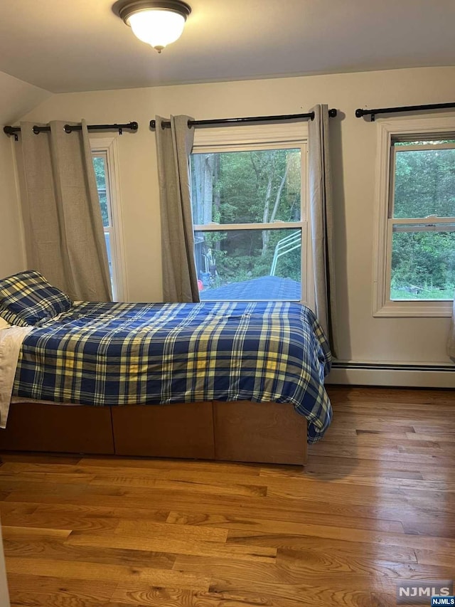 unfurnished bedroom featuring hardwood / wood-style floors, baseboard heating, and vaulted ceiling