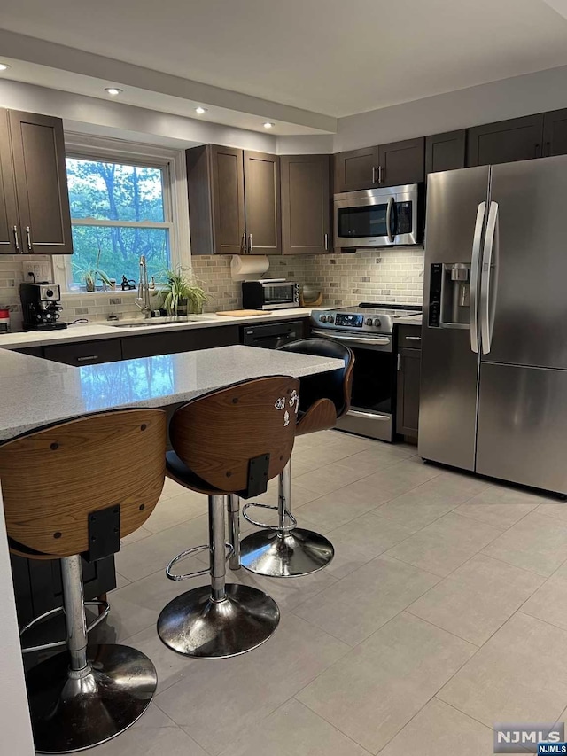 kitchen with dark brown cabinetry, decorative backsplash, sink, and appliances with stainless steel finishes