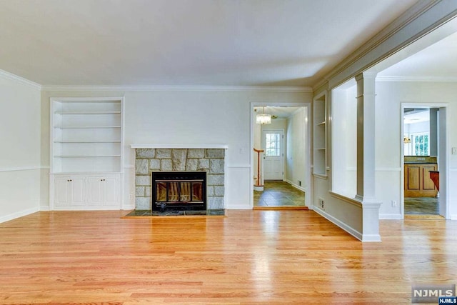 unfurnished living room with light wood-type flooring, built in features, crown molding, and a stone fireplace