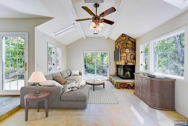 living room featuring vaulted ceiling with skylight, a stone fireplace, a wealth of natural light, and ceiling fan