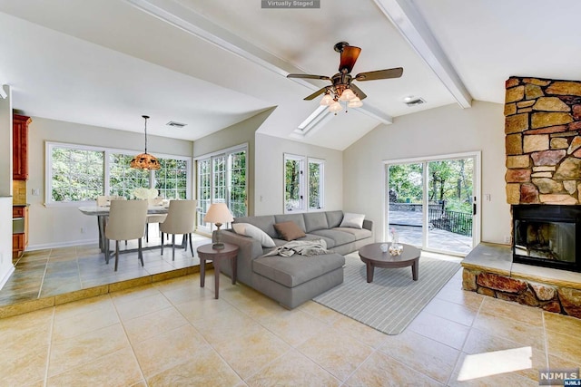 living room with vaulted ceiling with beams, a healthy amount of sunlight, a stone fireplace, and ceiling fan