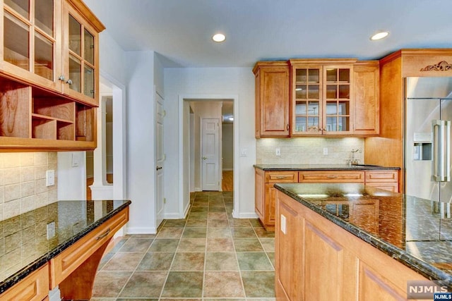 kitchen featuring built in fridge, dark stone counters, and tasteful backsplash