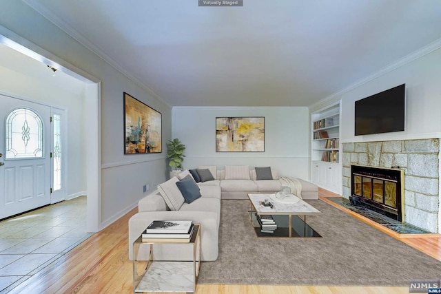 living room with light hardwood / wood-style floors, built in features, a stone fireplace, and crown molding