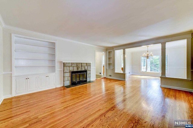 unfurnished living room featuring light wood-type flooring, a fireplace, ornamental molding, built in features, and a chandelier