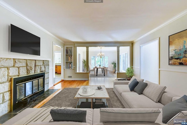 living room with a notable chandelier, wood-type flooring, a fireplace, and ornamental molding