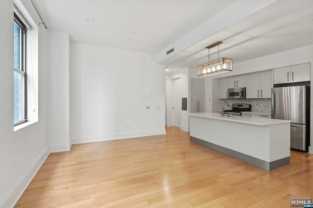 kitchen featuring decorative light fixtures, gray cabinets, stainless steel appliances, and light hardwood / wood-style flooring