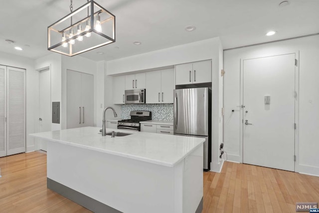 kitchen with pendant lighting, an island with sink, stainless steel appliances, and light wood-type flooring