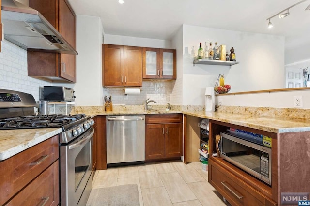 kitchen with sink, wall chimney exhaust hood, decorative backsplash, light stone countertops, and appliances with stainless steel finishes