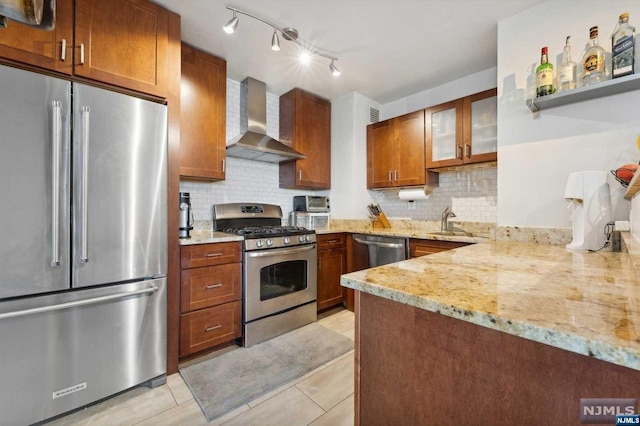 kitchen with light stone countertops, appliances with stainless steel finishes, decorative backsplash, wall chimney range hood, and light tile patterned floors