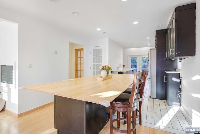 kitchen featuring french doors, stainless steel fridge, light hardwood / wood-style floors, a breakfast bar, and dark brown cabinets