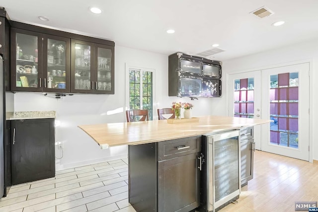 kitchen featuring dark brown cabinetry, a center island, french doors, beverage cooler, and light hardwood / wood-style flooring