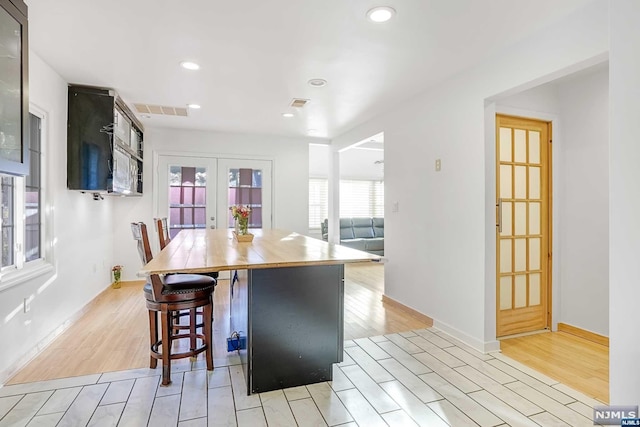 kitchen featuring french doors, light wood-type flooring, a kitchen island, and a kitchen breakfast bar