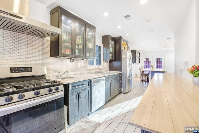 kitchen with french doors, appliances with stainless steel finishes, dark brown cabinetry, sink, and wall chimney range hood