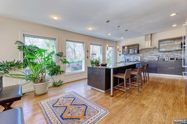 kitchen featuring a wealth of natural light, light hardwood / wood-style floors, an island with sink, and hanging light fixtures