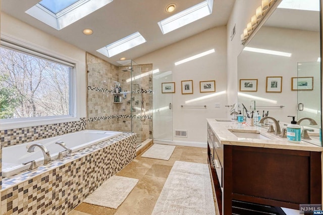 bathroom featuring vanity, independent shower and bath, and vaulted ceiling with skylight