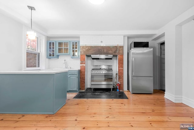 kitchen featuring hanging light fixtures, light wood-type flooring, range hood, and appliances with stainless steel finishes